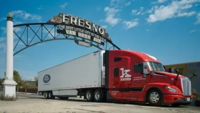 A red Kodiak AI autonomous semi-truck drives beneath the historic Fresno arch sign.