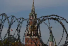 Barbed wire coils blur the view of the historic Moscow Kremlin tower and clock in Russia.