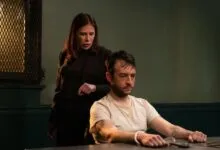 Maura Tierney standing behind a handcuffed suspect in an interrogation room