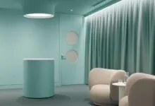 Modern interior featuring mint green walls, a cylindrical reception desk, and soft beige armchairs.