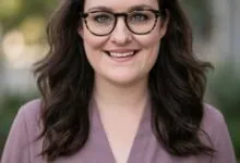 Professional headshot of Olivia Moore wearing glasses and a purple top with a soft, blurred background.
