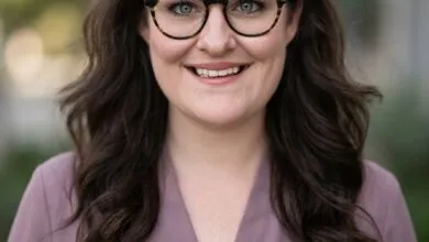 Professional headshot of Olivia Moore wearing glasses and a purple top with a soft, blurred background.