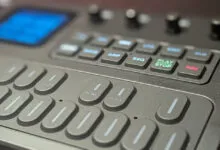 Close-up of a modern dark synthesizer keyboard with glowing blue, green, and red buttons and knobs.