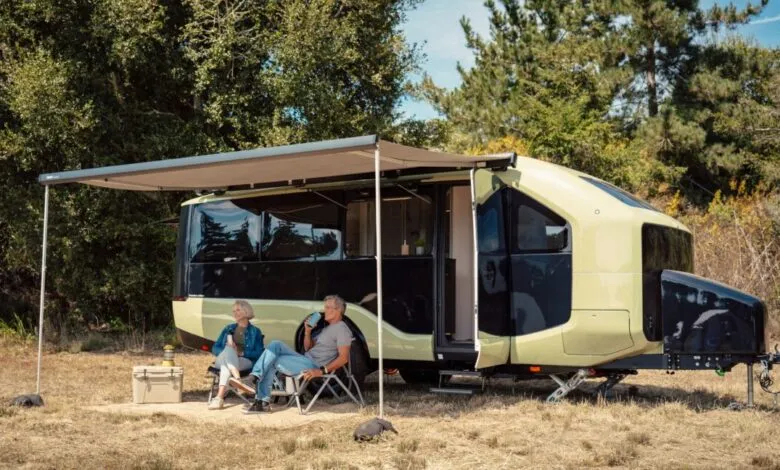 An older couple relaxing in camping chairs under the awning of a modern green and black RV.