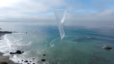 A white tapered balloon floating above a rocky coastline and blue ocean under a cloudy sky.