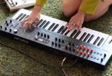 Close-up of hands playing an Arturia keyboard synthesizer on a green textured carpet.