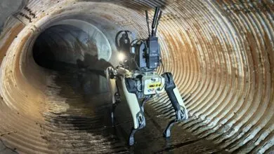 A quadruped robotic dog explores a dark, corrugated metal drainage pipe filled with water.