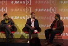 Three men seated on stage in modern chairs during a panel discussion at the HUMAN[X] conference.