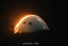 A glowing, dome-shaped white creature with dark eyes emerges from darkness, backlit by warm light.