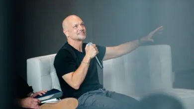 Tech innovator Tony Fadell speaking on a panel while holding a microphone and gesturing with his hand.