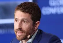 Tristan Harris speaking at a conference wearing a blue suit and a microphone headset