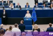 Ursula von der Leyen speaking at a blue podium in the European Parliament with EU flag.