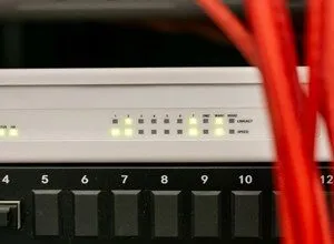 Close-up of a white network switch with blinking green lights and red cables in the foreground.