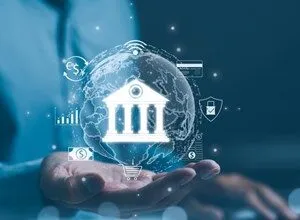 A person holds glowing digital banking icons and a globe in their hands above a laptop.