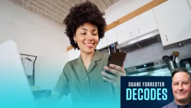 A smiling woman with dark curly hair looks at her smartphone in a modern kitchen.