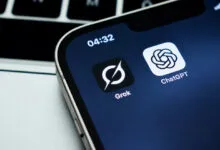 Smartphone screen displaying Grok and ChatGPT AI application icons next to a laptop keyboard.
