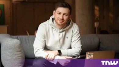Alex Ilyash sitting on a gray sofa in a modern office, wearing a light gray hoodie and smiling.