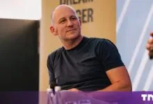 Allen Taylor wearing a navy t-shirt while seated on a conference stage