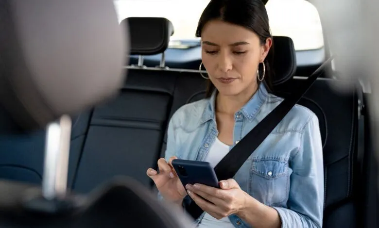 Woman in backseat of car looking at smartphone with a feeling of motion sickness
