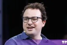 Anthropic CEO Dario Amodei speaking at an industry conference wearing glasses and a blue shirt