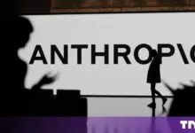 Silhouettes of people stand before a large screen displaying the Anthropic company logo in bold letters.