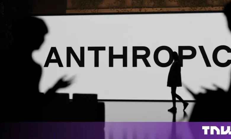Silhouettes of people stand before a large screen displaying the Anthropic company logo in bold letters.