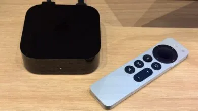 Black Apple TV 4K box with shiny top surface and silver Siri Remote placed on a wooden surface.