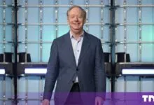 Microsoft President Brad Smith smiling on stage against a glowing blue geometric backdrop