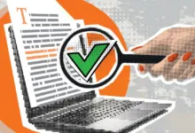 A hand holds a magnifying glass over a document on a laptop, revealing a green checkmark.