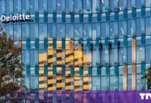 Modern glass facade of a Deloitte office building with reflective windows and corporate signage.