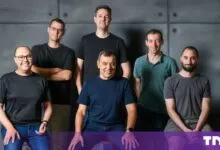 Group portrait of the six male cofounders of Double.ai posing against a dark grey panel wall.
