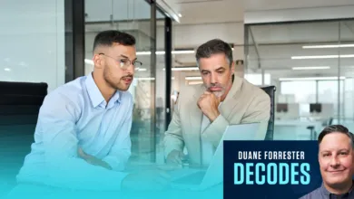 Two businessmen collaborating on a laptop inside a modern glass-walled corporate office.