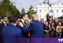 Donald Trump in a blue suit embraces Elon Musk in a black suit outside the White House with press.