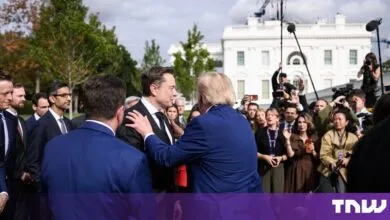 Donald Trump in a blue suit embraces Elon Musk in a black suit outside the White House with press.