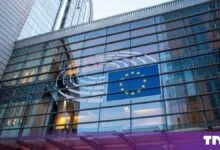 Modern glass facade of the European Parliament in Brussels displaying the EU flag and parliament symbol