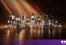 A diverse lineup of humanoid and quadruped robots standing in a warm, dimly lit studio.