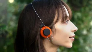 A young woman wearing orange on-ear headphones with a minimalist metal headband outdoors.
