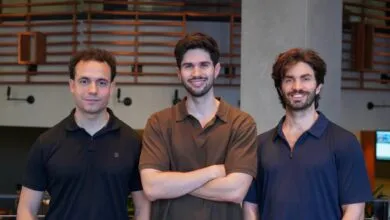 Three young male cofounders stand side-by-side smiling in a modern office interior.