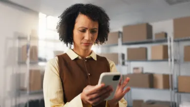 A warehouse worker with a concerned expression looks at her smartphone.