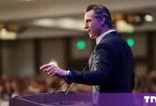 California Governor Gavin Newsom speaking passionately at a lectern before a blurred audience.