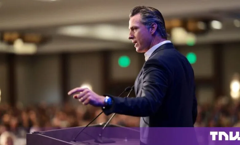 California Governor Gavin Newsom speaking passionately at a lectern before a blurred audience.