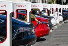 Row of Tesla vehicles plugged in and charging at a row of white and red Tesla Superchargers.