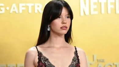 Actress Mia Goth attends a red carpet event wearing a dark lace dress and dangling earrings.