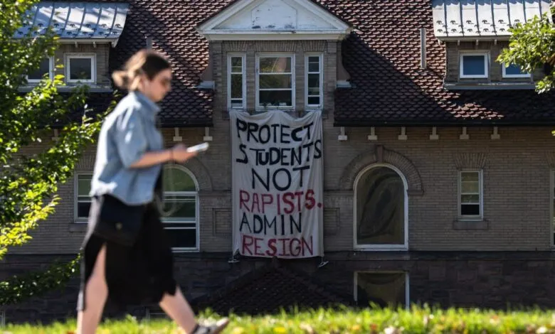A student walks past a university building displaying a protest banner reading Protect Students Not Rapists