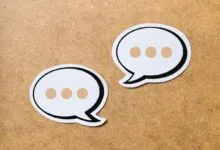 Two paper speech bubbles with three dots each resting on a textured wooden background.