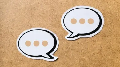 Two paper speech bubbles with three dots each resting on a textured wooden background.
