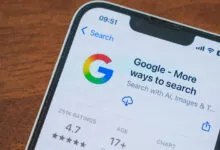 Smartphone displaying the Google app page with search options and a 4.7 star rating on a wooden table.