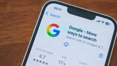 Smartphone displaying the Google app page with search options and a 4.7 star rating on a wooden table.