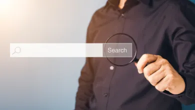 A person in a dark shirt holds a magnifying glass over a digital search bar.