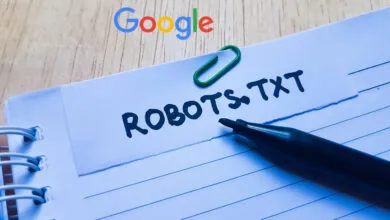 Robots.txt handwritten on paper note attached with green paperclip on a wooden desk with Google logo above